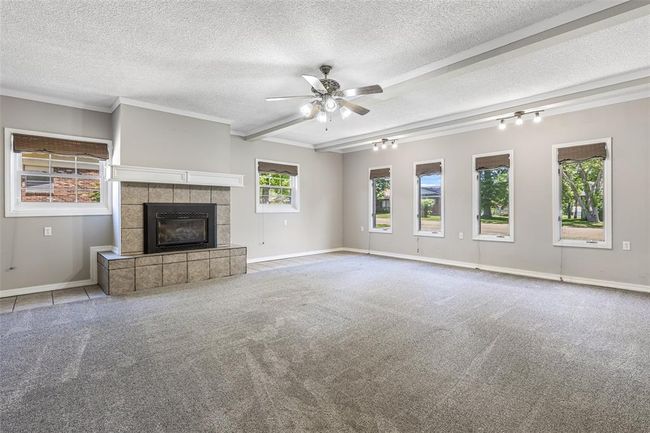 Unfurnished living room with a textured ceiling, a tiled fireplace, ceiling fan, baseboards, and carpet floors | Image 41