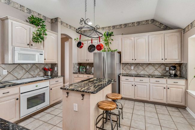 Kitchen featuring appliances, light tile patterned floors, a kitchen island, a breakfast bar area, and decorative backsplash. Countertops are marble. | Image 13