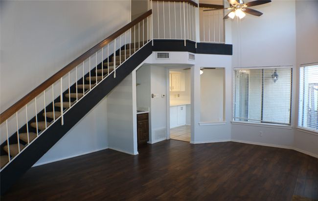 Unfurnished living room featuring stairs, a ceiling fan, wood finished floors, and a towering ceiling | Image 12