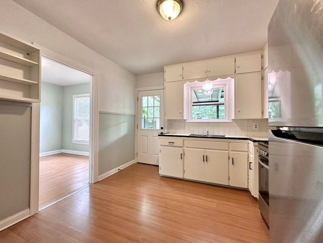Kitchen with freestanding refrigerator, light wood-style floors, white cabinetry, and decorative backsplash | Image 19