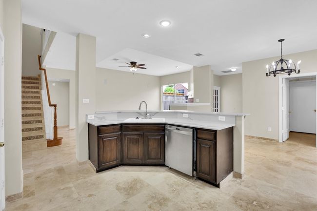 Kitchen with stainless steel dishwasher, a sink, ceiling fan with notable chandelier, dark brown cabinetry, and light countertops | Image 15