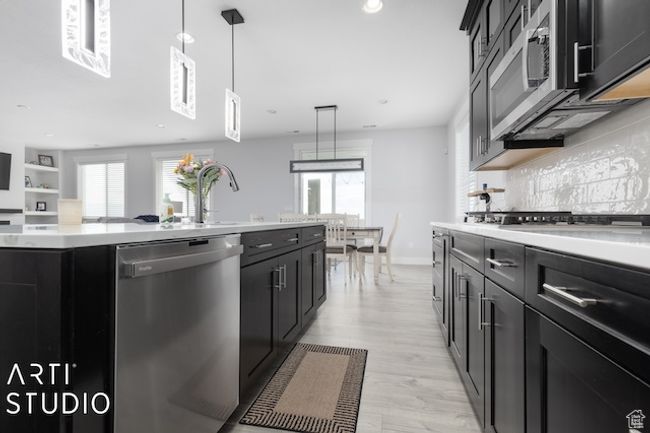 Kitchen featuring an island with sink, dark cabinetry, appliances with stainless steel finishes, light countertops, and decorative backsplash | Image 14
