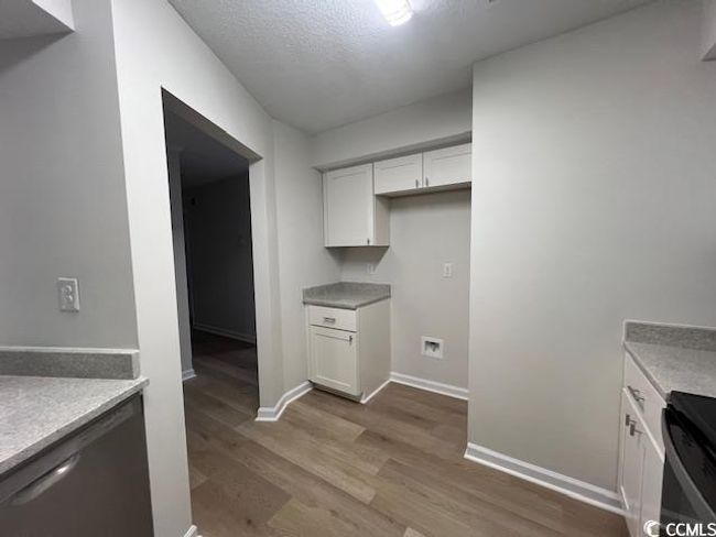 Kitchen featuring stainless steel dishwasher, wood finished floors, baseboards, light countertops, and white cabinets | Image 27