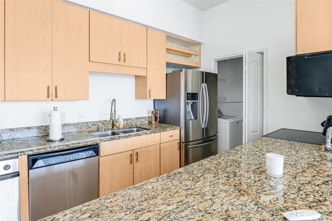 Kitchen featuring stainless steel appliances, washer / dryer, light brown cabinetry, light stone countertops, and open shelves | Image 18