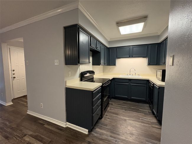 Kitchen with crown molding, light countertops, black appliances, and dark wood finished floors | Image 8