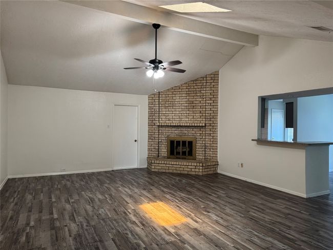 Unfurnished living room featuring dark wood-style flooring, beamed ceiling, a ceiling fan, a brick fireplace, and baseboards | Image 12