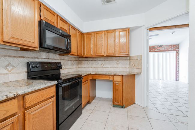 Kitchen featuring tasteful backsplash, light stone counters, light tile patterned flooring, visible vents, and black appliances | Image 5