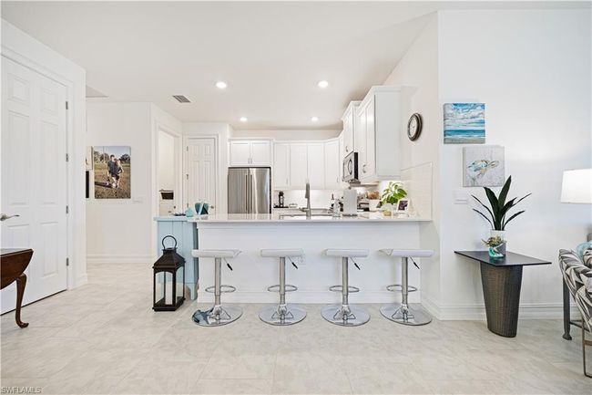 Kitchen with appliances with stainless steel finishes, a peninsula, a kitchen bar, white cabinets, and light countertops | Image 6