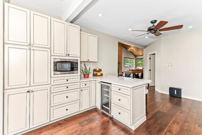 Kitchen with stainless steel microwave, a peninsula, beverage cooler, light countertops, and dark wood finished floors | Image 10