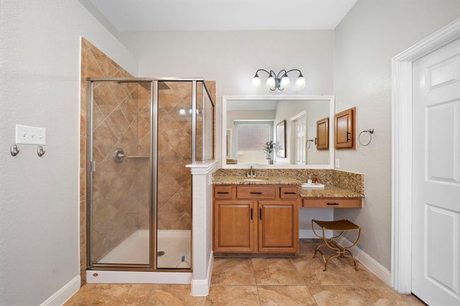 The ensuite bath offers a glass-enclosed shower with elegant tile work and dual granite vanities, blending functionality with luxury. Light wooden cabinetry provides ample storage, while a stylish vanity area adds a touch of elegance to this serene retreat. | Image 31