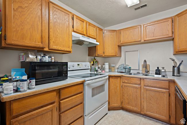 Kitchen featuring white electric stove, under cabinet range hood, stainless steel dishwasher, light countertops, and light tile patterned floors | Image 38