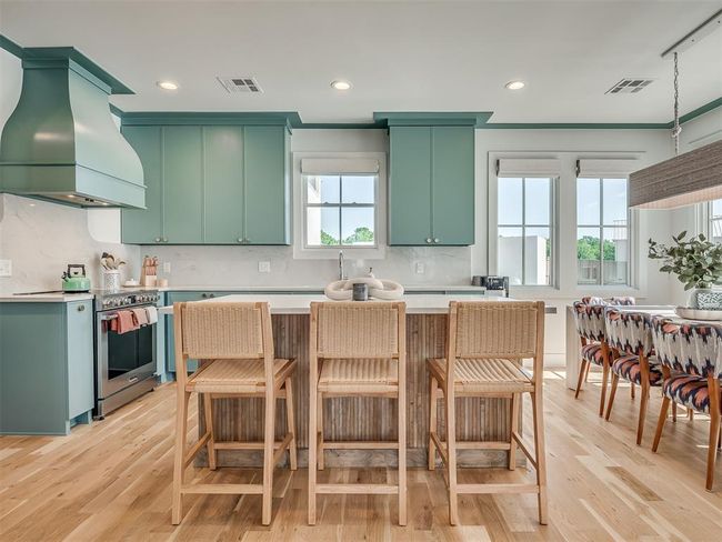 Kitchen featuring high end range, custom range hood, green cabinetry, light wood finished floors, and light countertops | Image 12