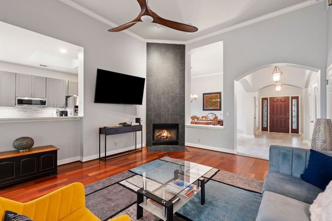 Living room featuring arched walkways, a tiled fireplace, wood finished floors, ceiling fan, and ornamental molding | Image 8
