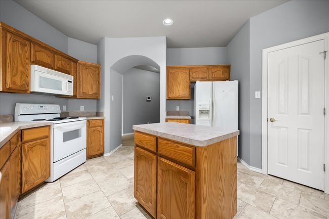 Kitchen featuring white appliances, arched walkways, light countertops, a kitchen island, and brown cabinets | Image 8
