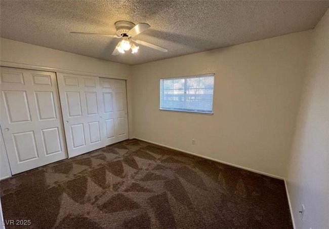 Unfurnished bedroom featuring dark carpet, a closet, a textured ceiling, a ceiling fan, and baseboards | Image 8