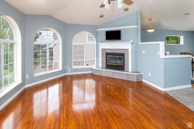 Unfurnished living room with a wealth of natural light, a tiled fireplace, ceiling fan, and hardwood / wood-style flooring | Image 4
