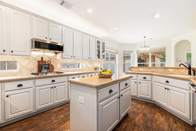 A light and bright island kitchen boasts freshly painted, crisp white cabinets providing storage, and quartz countertops for clean prep space! | Image 19