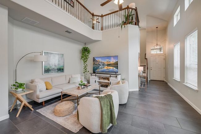 Living room featuring a high ceiling, dark tile patterned floors, plenty of natural light, ceiling fan, and baseboards | Image 12
