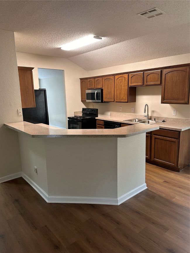 Kitchen with stove, a sink, refrigerator, dark wood finished floors, and lofted ceiling | Image 5