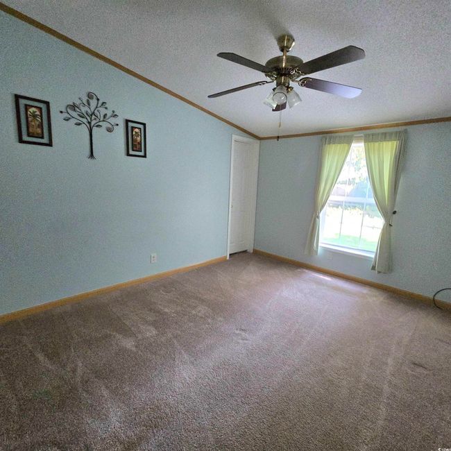 Empty room with crown molding, a textured ceiling, a ceiling fan, and carpet | Image 12