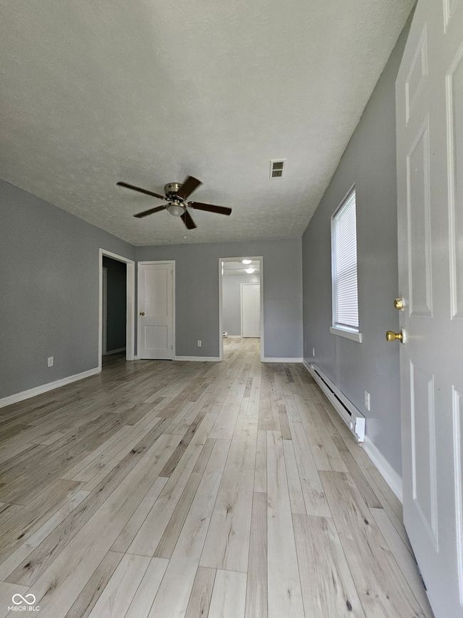 empty room with baseboard heating, ceiling fan, light wood-style floors, baseboards, and a textured ceiling | Image 10