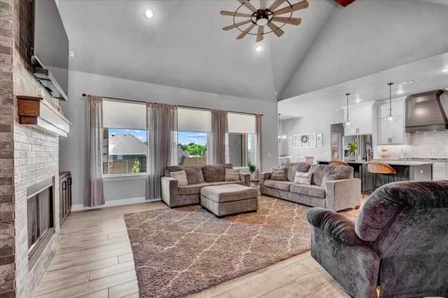 Living area featuring a ceiling fan, high vaulted ceiling, light wood-type flooring, a brick fireplace, and recessed lighting | Image 14