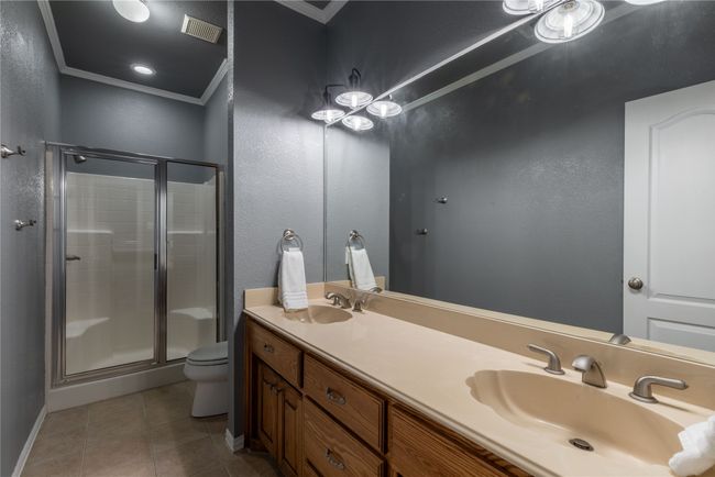 Full bathroom with crown molding, a shower stall, double vanity, tile patterned floors, and a textured wall | Image 30