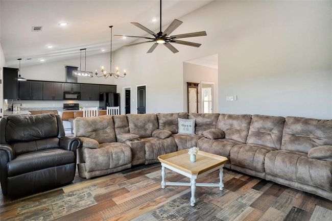 Living room featuring high vaulted ceiling, ceiling fan with notable chandelier, and wood-type flooring | Image 6