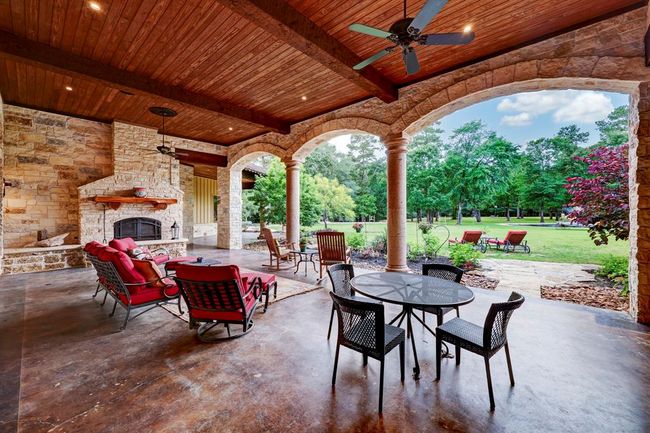 The outdoor covered patio has ample seating room, ceiling fans, and an outdoor wood burning fireplace. | Image 39