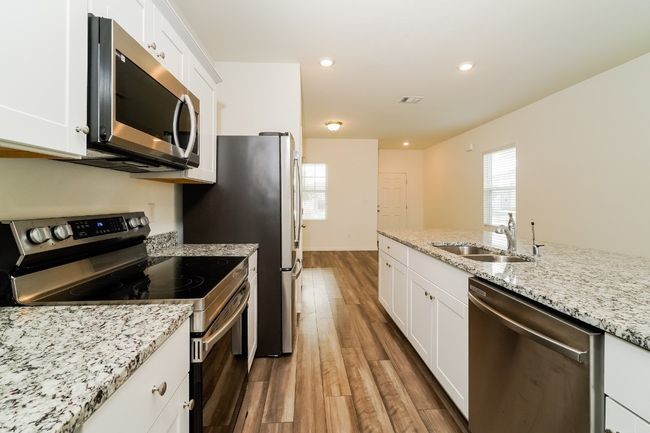 Kitchen featuring appliances with stainless steel finishes, wood finished floors, white cabinets, light stone counters, and recessed lighting | Image 10