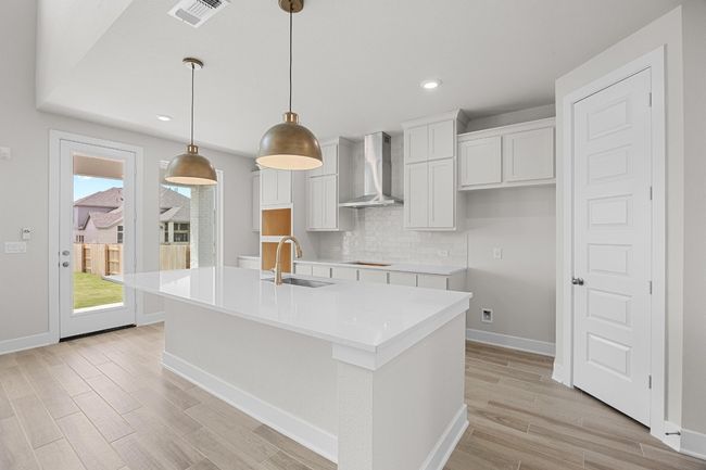 Kitchen featuring wall chimney exhaust hood, a sink, backsplash, light wood-type flooring, and an island with sink | Image 9