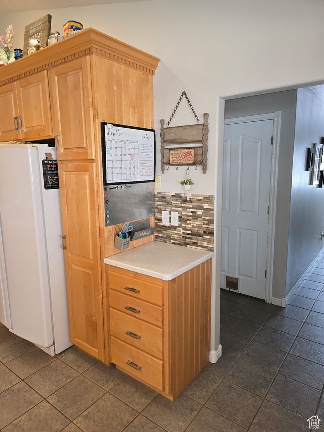 Kitchen featuring freestanding refrigerator, visible vents, light countertops, dark tile patterned floors, and backsplash | Image 26
