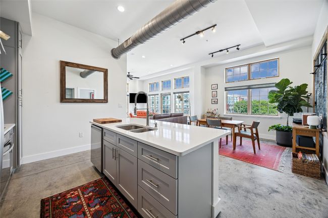 Kitchen with gray cabinetry, finished concrete floors, light countertops, stainless steel dishwasher, and a center island with sink | Image 11