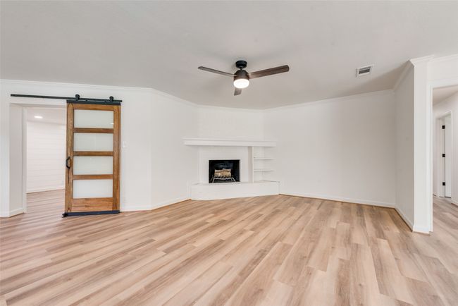 Unfurnished living room with ceiling fan, a barn door, light wood-style floors, crown molding, and a fireplace with raised hearth | Image 9