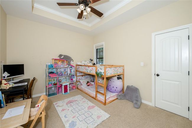 Carpeted bedroom featuring baseboards, a raised ceiling, a ceiling fan, and ornamental molding | Image 25