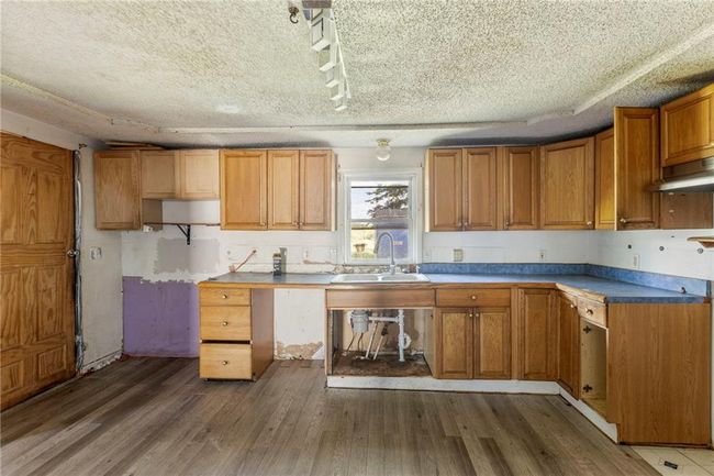 Kitchen with wood finished floors, brown cabinets, a textured ceiling, and under cabinet range hood | Image 12