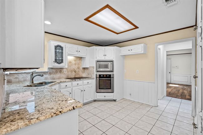 Kitchen featuring stainless steel appliances, white cabinetry, light tile patterned floors, crown molding, and wainscoting | Image 7