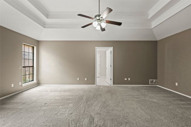 Carpeted empty room with a raised ceiling, ornamental molding, and ceiling fan | Image 23