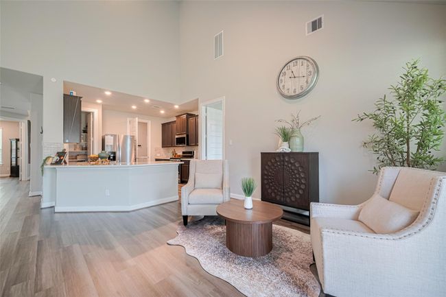 This photo showcases a bright, open-plan living space with high ceilings, featuring a modern kitchen with dark cabinets and stainless steel appliances and kitchen island | Image 15