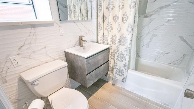 Full bath featuring shower / bathtub combination with curtain, vanity, toilet, tile walls, and wood finished floors | Image 4