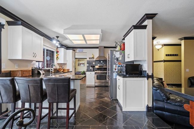 Kitchen with stainless steel appliances, wall chimney exhaust hood, dark countertops, a peninsula, and white cabinetry | Image 11