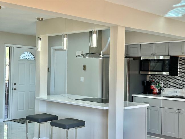 Kitchen featuring wall chimney range hood, stainless steel microwave, tasteful backsplash, gray cabinetry, and black electric cooktop | Image 19