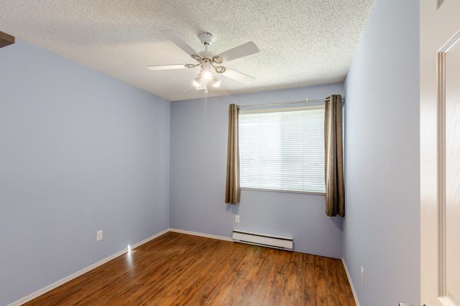 Bedroom with a textured ceiling, baseboard heating, wood finished floors, and a ceiling fan | Image 25