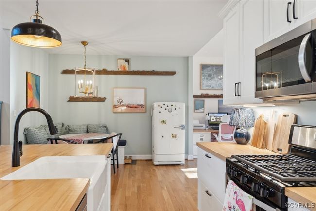 Kitchen with light wood-type flooring, butcher block countertops, a sink, stainless steel appliances, and white cabinets | Image 13