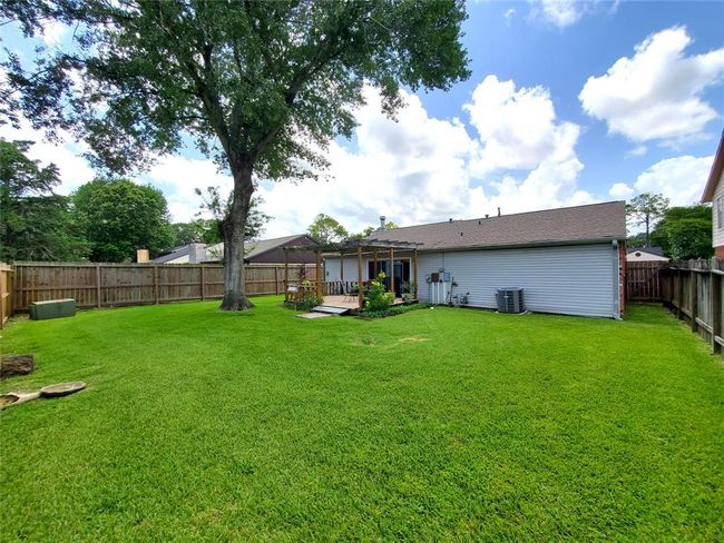 Spacious backyard with a large tree, a well-maintained lawn, and a wooden fence for privacy. The house features a covered patio area, perfect for outdoor relaxation and entertaining. | Image 12
