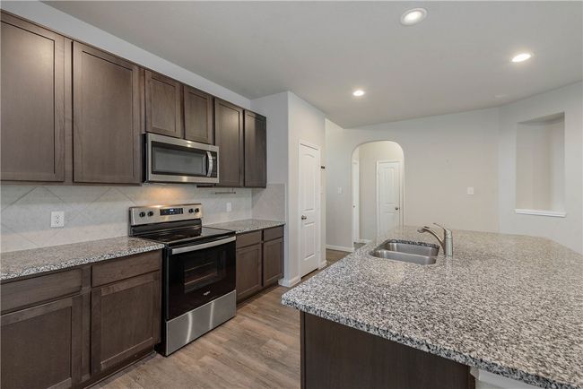 Kitchen featuring appliances with stainless steel finishes, arched walkways, light wood finished floors, light stone countertops, and recessed lighting | Image 6
