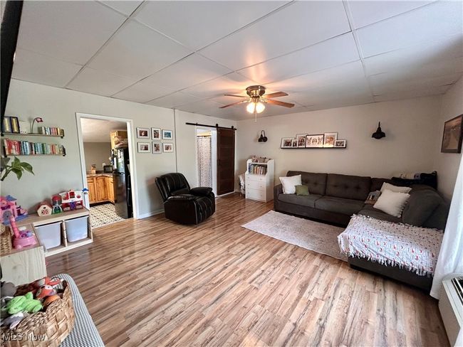 Living area with a barn door, ceiling fan, wood finished floors, a paneled ceiling, and baseboards | Image 4
