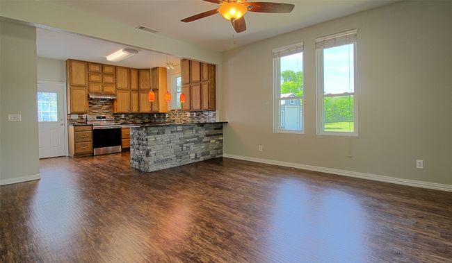 Kitchen featuring brown cabinets, stainless steel range with electric cooktop, visible vents, and dark wood-type flooring | Image 4