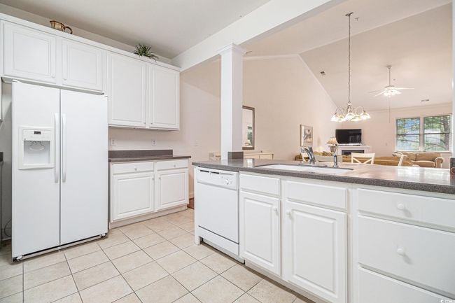 Kitchen with white appliances, a sink, dark countertops, light tile patterned floors, and lofted ceiling | Image 10