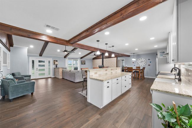 Kitchen with open floor plan, dark wood-type flooring, beam ceiling, a breakfast bar area, and white cabinets | Image 7